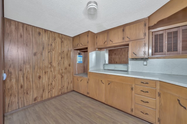 17230 Pioneer Trl, Conroe, TX 77302 - kitchen with a textured ceiling, light wood-type flooring, light countertops, wooden walls, and brown cabinetry