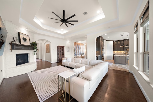 28106 Island Manor Ln, Fulshear, TX 77441 - living area with arched walkways, a ceiling fan, a tray ceiling, dark wood-style floors, and ornamental molding