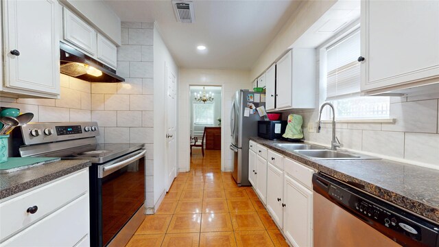 9030 Troulon Dr, Houston, TX 77036 - kitchen with appliances with stainless steel finishes, dark countertops, under cabinet range hood, light tile patterned floors, and white cabinetry