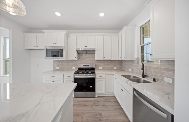 31727 Valor Dr, Fulshear, TX 77441 - kitchen with stainless steel appliances, under cabinet range hood, white cabinets, light wood-style floors, and light stone countertops