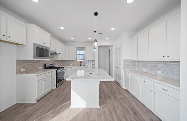 31727 Valor Dr, Fulshear, TX 77441 - kitchen featuring appliances with stainless steel finishes, under cabinet range hood, light wood-style flooring, white cabinets, and backsplash