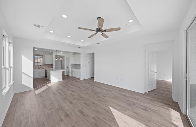 31727 Valor Dr, Fulshear, TX 77441 - unfurnished living room featuring a tray ceiling, a ceiling fan, recessed lighting, and light wood-type flooring