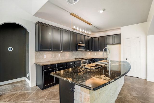16206 Lakewood Field Dr, Tomball, TX 77377 - kitchen with appliances with stainless steel finishes, dark stone counters, backsplash, arched walkways, and a kitchen island with sink