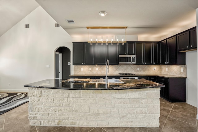 16206 Lakewood Field Dr, Tomball, TX 77377 - kitchen featuring stainless steel microwave, dark stone countertops, arched walkways, and a center island with sink