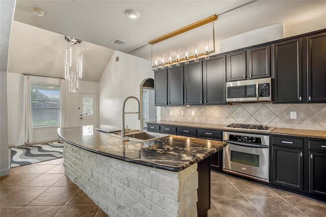 16206 Lakewood Field Dr, Tomball, TX 77377 - kitchen featuring appliances with stainless steel finishes, arched walkways, tasteful backsplash, dark tile patterned flooring, and an island with sink