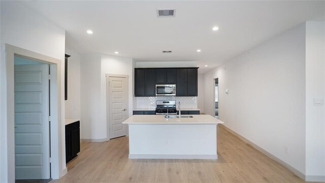30106 Reagans Ranch Dr, Katy, TX 77494 - kitchen with appliances with stainless steel finishes, dark cabinetry, light countertops, decorative backsplash, and a center island with sink