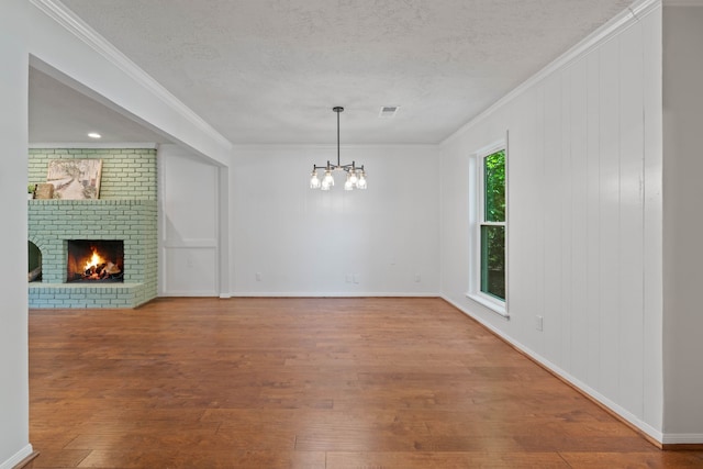 10813 Colony Wood Pl, The Woodlands, TX 77380 - unfurnished living room with crown molding, a chandelier, wood finished floors, a fireplace, and a textured ceiling