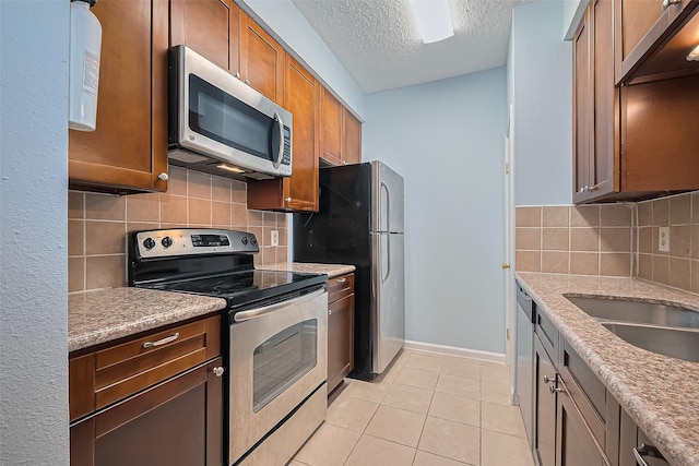 7900 N Stadium Dr Unit 123, Houston, TX 77030 - kitchen featuring appliances with stainless steel finishes, a textured ceiling, light tile patterned floors, decorative backsplash, and brown cabinetry