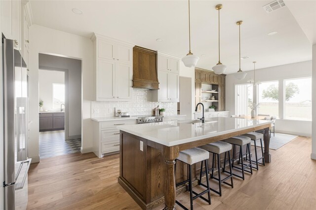 1355 Bluebonnet Ridge Dr, Chappell Hill, TX 77426 - kitchen with custom exhaust hood, stainless steel refrigerator, light wood finished floors, tasteful backsplash, and white cabinets