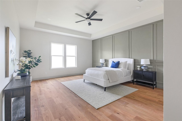 1355 Bluebonnet Ridge Dr, Chappell Hill, TX 77426 - bedroom featuring a tray ceiling, light wood-style flooring, a decorative wall, and a ceiling fan