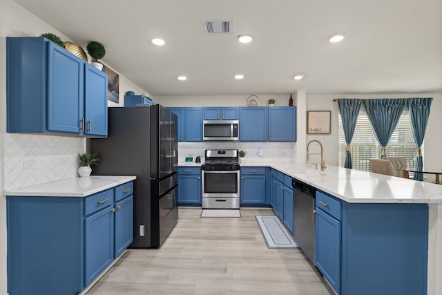 10433 Russell Pines Dr, Rosharon, TX 77583 - kitchen featuring stainless steel appliances, a peninsula, backsplash, blue cabinetry, and light wood finished floors