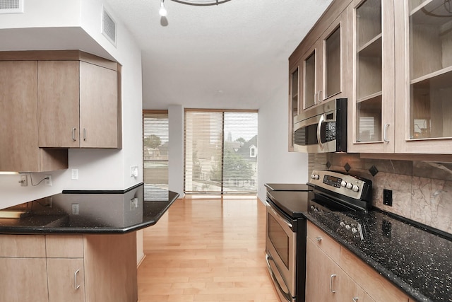 1111 Bering Dr Unit 306, Houston, TX 77057 - kitchen with appliances with stainless steel finishes, a wall of windows, light wood-style flooring, decorative backsplash, and dark stone countertops