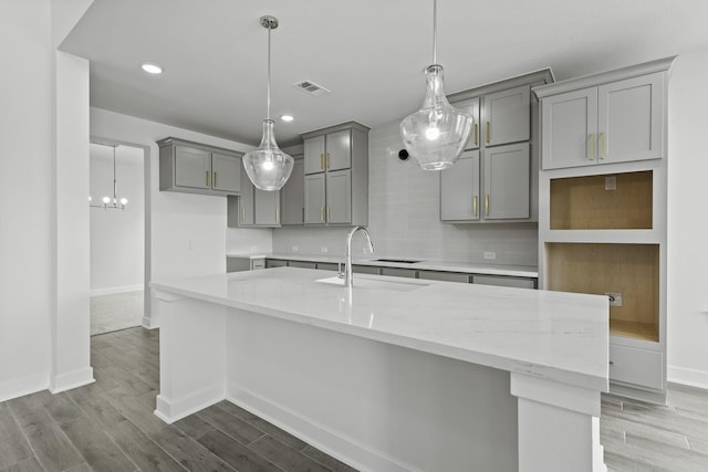 5029 Steady Breeze Dr, Katy, TX 77493 - kitchen featuring gray cabinets, an island with sink, wood finished floors, tasteful backsplash, and light stone counters