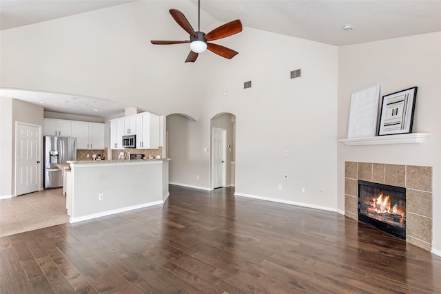 19002 Volley Vale Ct, Humble, TX 77346 - unfurnished living room featuring ceiling fan, high vaulted ceiling, wood finished floors, arched walkways, and a tile fireplace