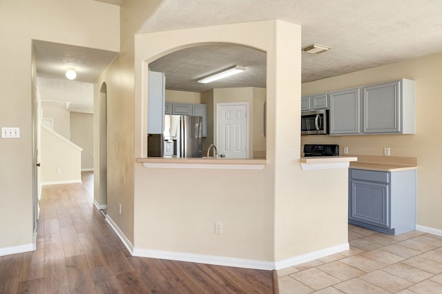 3434 Fiorella Way, Humble, TX 77338 - kitchen with stainless steel appliances, gray cabinetry, arched walkways, a textured ceiling, and light countertops