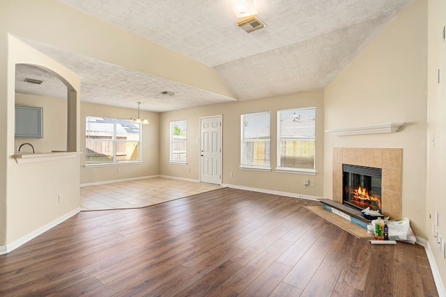 3434 Fiorella Way, Humble, TX 77338 - unfurnished living room featuring a textured ceiling, wood-type flooring, a chandelier, a tile fireplace, and vaulted ceiling