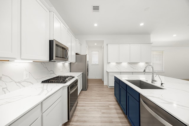 15308 Sandhill Crane Ln, Conroe, TX 77384 - kitchen with appliances with stainless steel finishes, white cabinets, blue cabinetry, recessed lighting, and light stone countertops