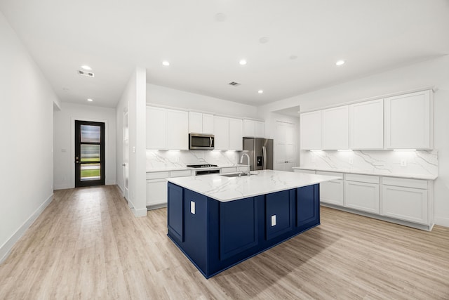 15308 Sandhill Crane Ln, Conroe, TX 77384 - kitchen featuring appliances with stainless steel finishes, light wood-style floors, a center island with sink, backsplash, and recessed lighting