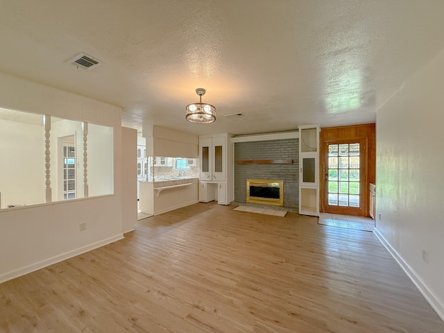 20 Woods Ln, Coldspring, TX 77331 - unfurnished living room with light wood finished floors, a chandelier, a textured ceiling, and a fireplace