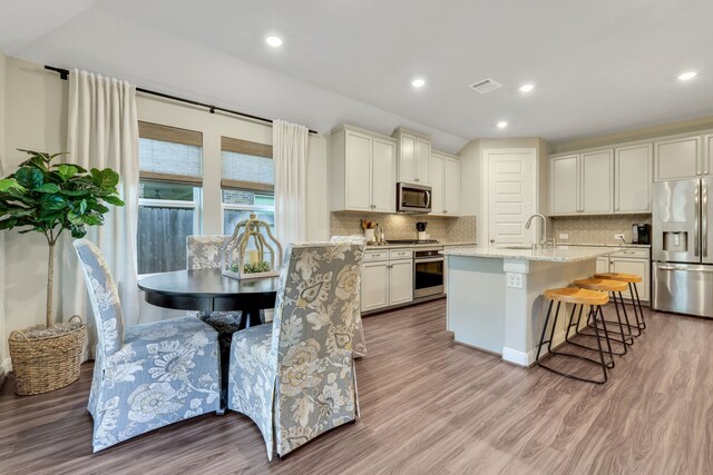 21310 Baldovin Way, Tomball, TX 77375 - kitchen with stainless steel appliances, light wood-style floors, backsplash, a kitchen island with sink, and recessed lighting