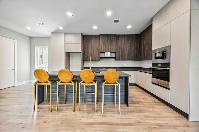 1111 W 21st St, Houston, TX 77008 - kitchen featuring stainless steel appliances, modern cabinets, wall chimney range hood, a breakfast bar area, and recessed lighting
