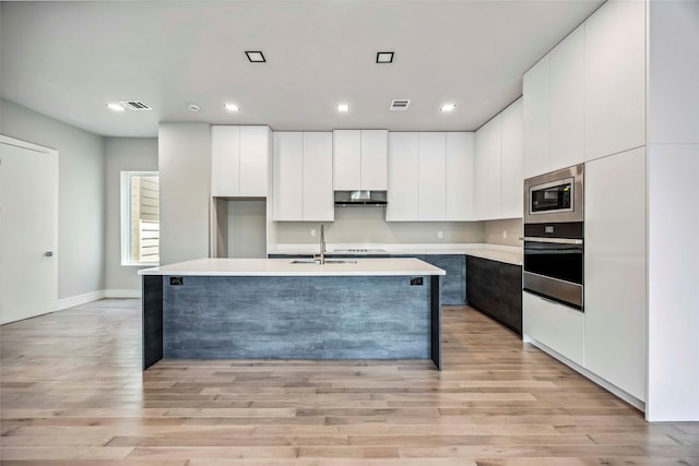 1111 W 21st St, Houston, TX 77008 - kitchen featuring appliances with stainless steel finishes, modern cabinets, an island with sink, white cabinets, and light wood-style floors
