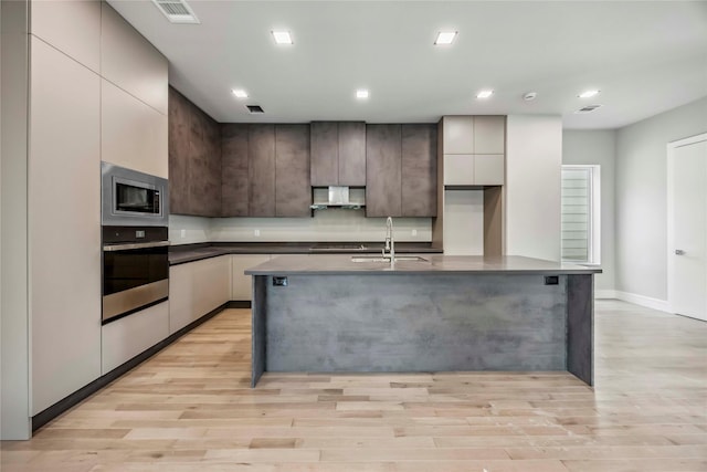 1111 W 21st St, Houston, TX 77008 - kitchen featuring appliances with stainless steel finishes, wall chimney range hood, light wood-type flooring, modern cabinets, and recessed lighting