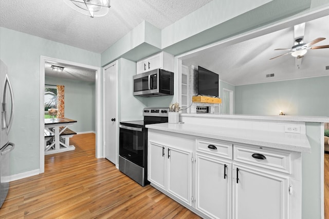 2014 17th St N, Texas City, TX 77590 - kitchen with stainless steel appliances, a textured ceiling, light wood-style flooring, white cabinets, and a peninsula