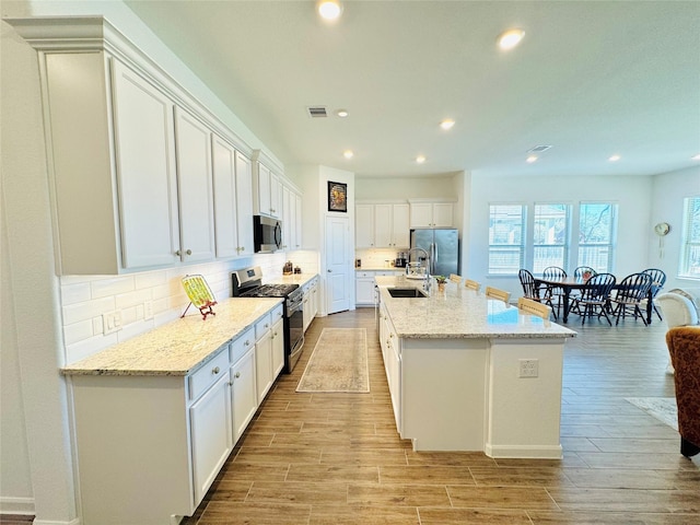 11119 Alpenhorn Pl, Tomball, TX 77375 - kitchen with stainless steel appliances, light wood-style floors, an island with sink, backsplash, and recessed lighting