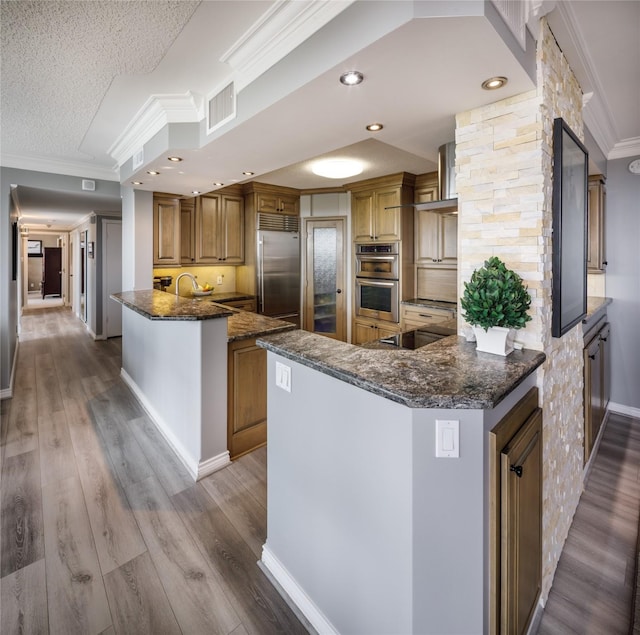 5001 Woodway Dr Unit 1704, Houston, TX 77056 - kitchen with stainless steel appliances, crown molding, a peninsula, dark stone counters, and brown cabinets