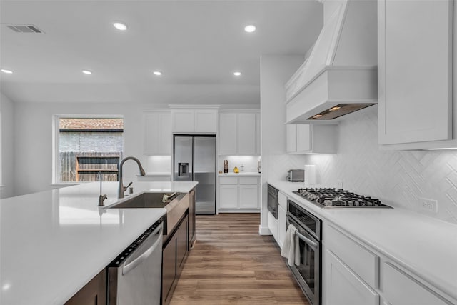 10614 Hazel Hills Dr, Cypress, TX 77433 - kitchen with custom exhaust hood, stainless steel appliances, light countertops, white cabinetry, and light wood finished floors