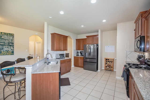 1911 Vineyard Bend Ct, Pearland, TX 77581 - kitchen featuring black appliances, arched walkways, a peninsula, a kitchen bar, and decorative backsplash