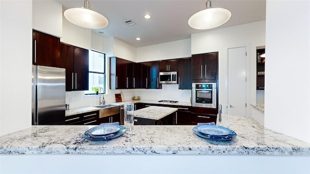 1767 Michigan St, Houston, TX 77006 - kitchen featuring appliances with stainless steel finishes, a center island, backsplash, hanging light fixtures, and light stone counters