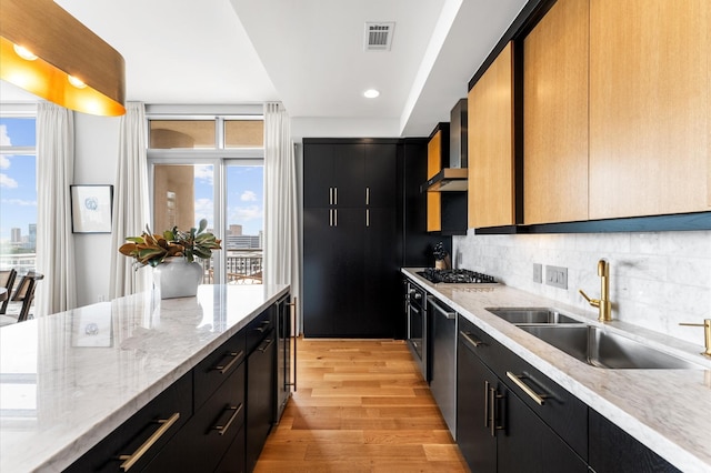 2207 Bancroft St Unit 1104, Houston, TX 77027 - kitchen featuring dark cabinets, light wood finished floors, decorative backsplash, wall chimney range hood, and plenty of natural light