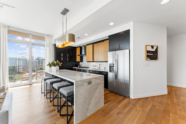 2207 Bancroft St Unit 1104, Houston, TX 77027 - kitchen with stainless steel appliances, wall chimney exhaust hood, a kitchen breakfast bar, light wood finished floors, and dark cabinetry