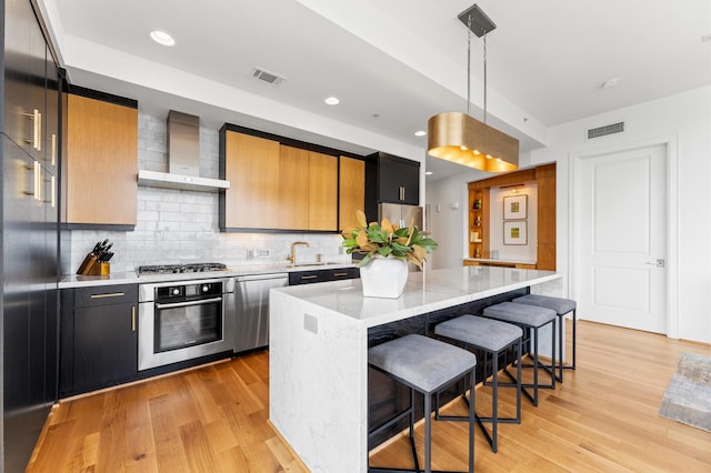 2207 Bancroft St Unit 1104, Houston, TX 77027 - kitchen featuring appliances with stainless steel finishes, wall chimney range hood, a breakfast bar, a center island, and decorative backsplash