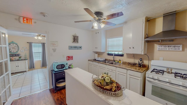 216 E Plantation Dr, Clute, TX 77531 - kitchen featuring wall chimney range hood, white appliances, a ceiling fan, white cabinets, and a textured ceiling