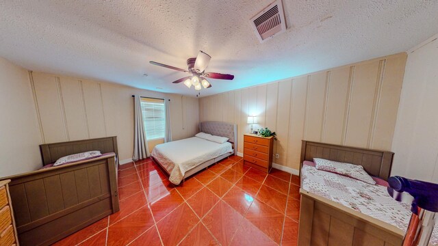 216 E Plantation Dr, Clute, TX 77531 - tiled bedroom featuring a ceiling fan, a decorative wall, and a textured ceiling