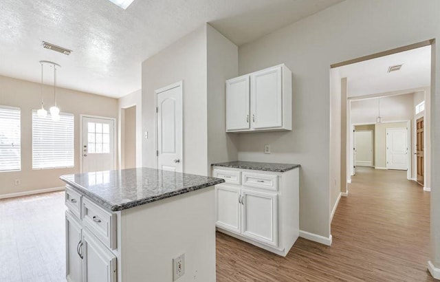 4611 Green Trail Dr, Houston, TX 77084 - kitchen with light wood-style floors, dark stone counters, white cabinetry, a kitchen island, and a textured ceiling