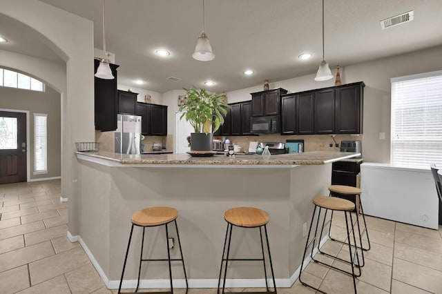 7455 Durango Creek Dr, Magnolia, TX 77354 - kitchen featuring black microwave, freestanding refrigerator, a breakfast bar area, light tile patterned floors, and range