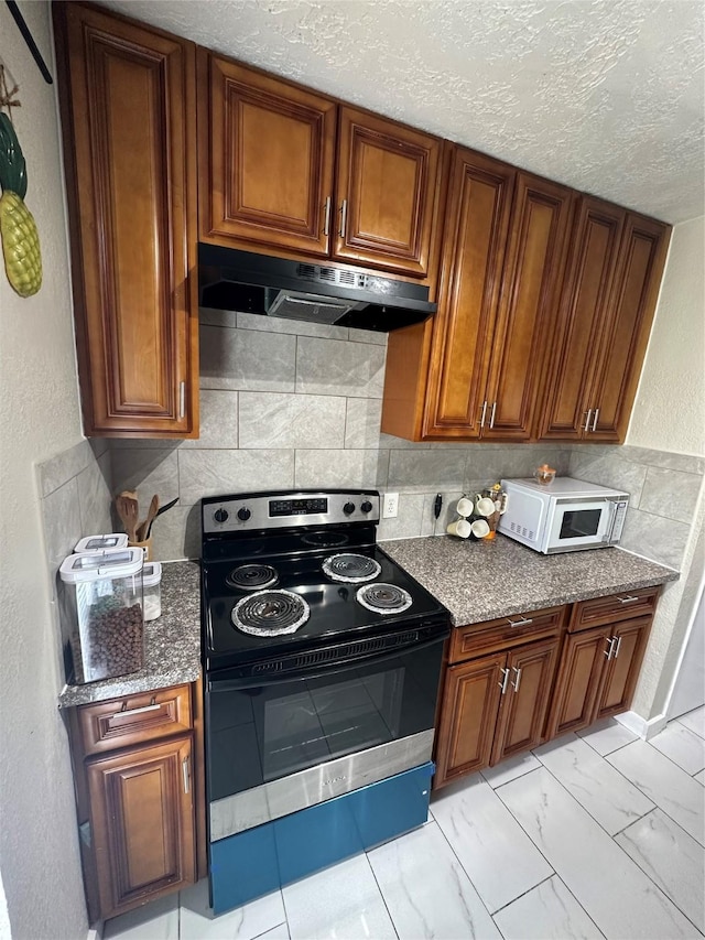 6618 Hopper Rd, Houston, TX 77016 - kitchen featuring stainless steel range with electric stovetop, under cabinet range hood, white microwave, brown cabinets, and dark stone countertops