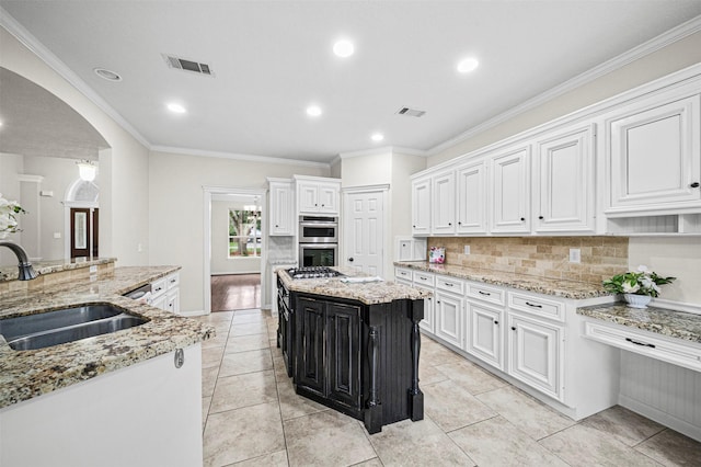2452 Ripplewood Dr, Conroe, TX 77384 - kitchen featuring appliances with stainless steel finishes, arched walkways, white cabinets, backsplash, and ornamental molding