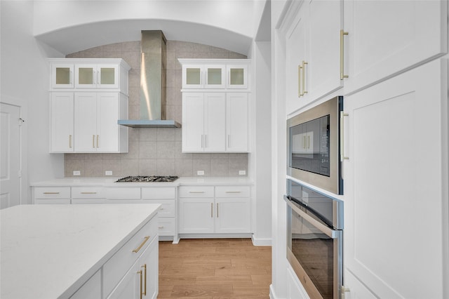 30218 Indigo Falls Dr, Brookshire, TX 77423 - kitchen featuring stainless steel appliances, wall chimney exhaust hood, light wood-style flooring, light countertops, and white cabinets