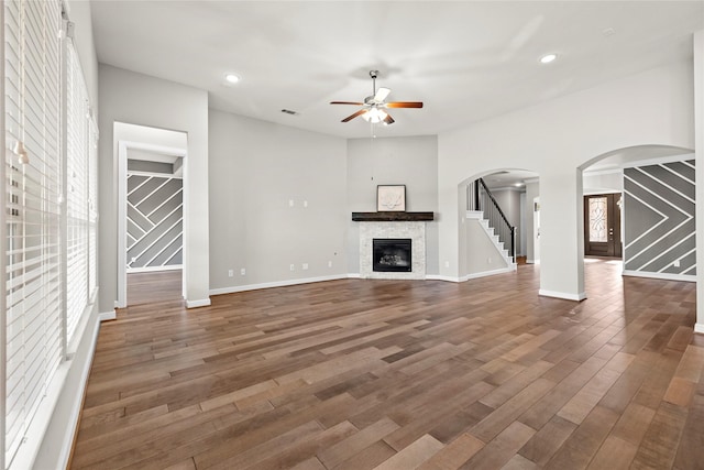 5715 Caper Shores Ln, Sugar Land, TX 77479 - unfurnished living room featuring ceiling fan, wood finished floors, a stone fireplace, stairs, and arched walkways
