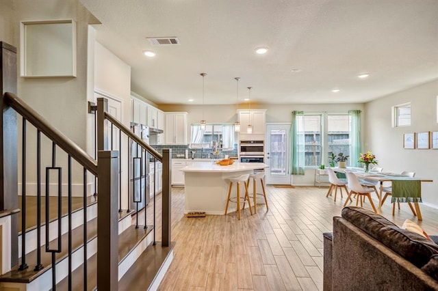 3226 Longleaf Meadows Dr, Houston, TX 77063 - kitchen featuring stainless steel double oven, white cabinets, a breakfast bar, light wood-style flooring, and decorative backsplash