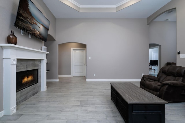 5 Corkwood Rd, Trinity, TX 75862 - living room featuring arched walkways, a tiled fireplace, a raised ceiling, ornamental molding, and light wood-style flooring