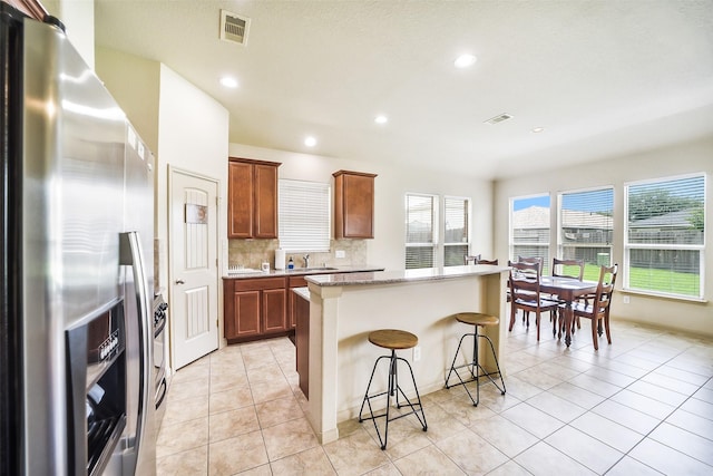 2614 Maverick Park Ln, Katy, TX 77449 - kitchen featuring stainless steel refrigerator with ice dispenser, a breakfast bar area, a kitchen island, light tile patterned floors, and brown cabinetry