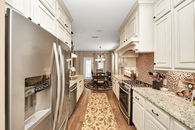 6111 Meadowstream Ct, Katy, TX 77450 - kitchen featuring stainless steel appliances, light wood finished floors, decorative backsplash, decorative light fixtures, and light stone countertops