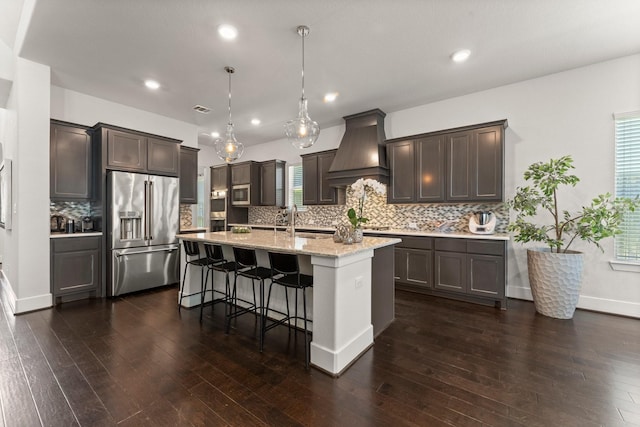 22 Mayapple Blossom Pl, Tomball, TX 77375 - kitchen with stainless steel appliances, custom exhaust hood, dark brown cabinets, a kitchen island with sink, and recessed lighting