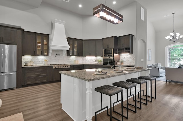 2172 Greentree Dr, Huntsville, TX 77340 - kitchen featuring stainless steel appliances, custom range hood, high vaulted ceiling, glass insert cabinets, and a kitchen bar
